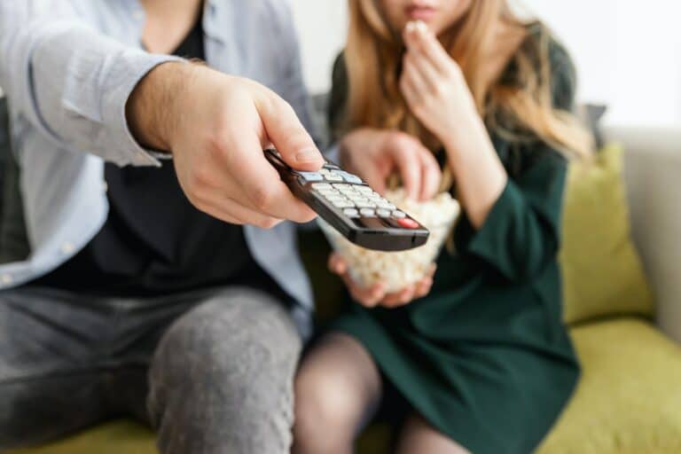 Imagem com foto de pessoas assistindo televisão apontando o controle remoto