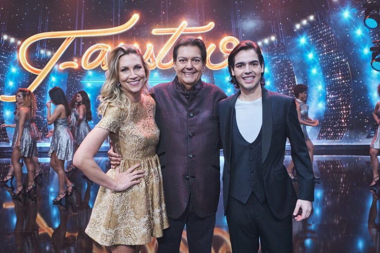 Imagem com foto de Anne Lottermann, Fausto Silva e João Guilherme Silva no palco do Faustão na Band