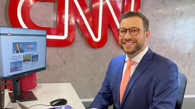 Imagem com foto do jornalista Cassius Zeilmann sentado em frente de um computador na Redação da CNN Brasil