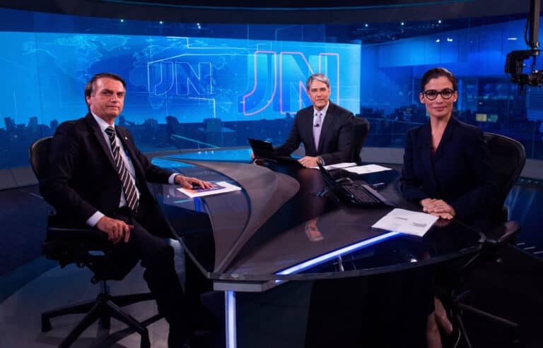 Imagem com foto de William Bonner e Renata Vasconcellos entrevistando Jair Bolsonaro no Jornal Nacional em 2018