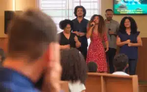 Solange canta toda a sua raiva e o seu desespero junto com o coral da igreja para Theo em Vai na Fé