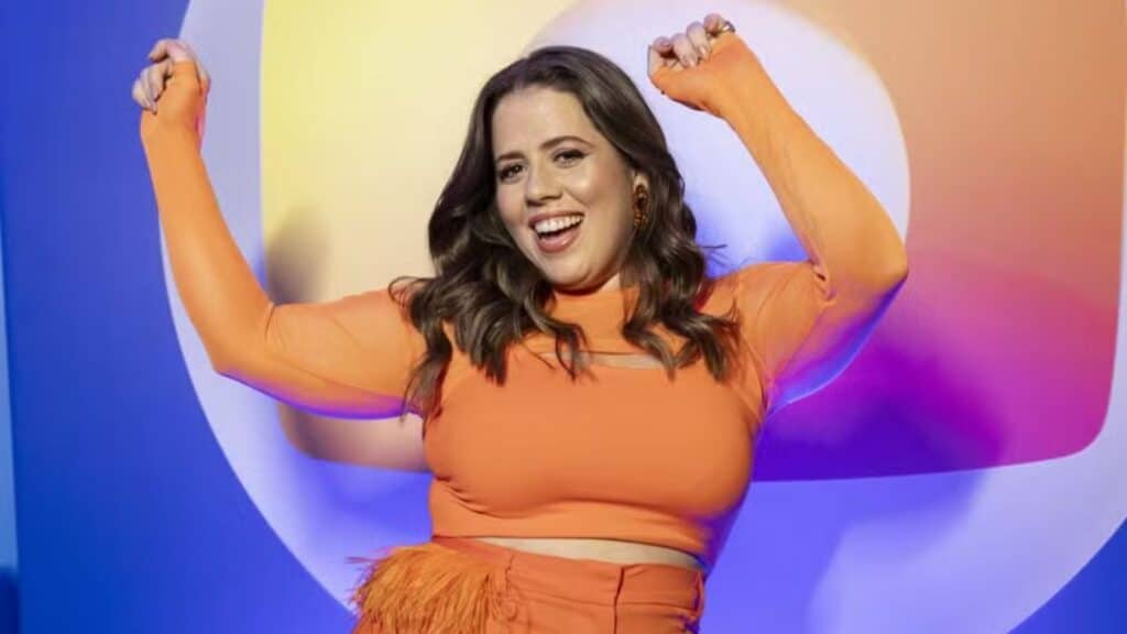 Foto de Tati Machado com logo da Globo ao fundo