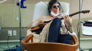 Foto de Branco Mello, do Titãs, segurando guitarra em cama de hospital