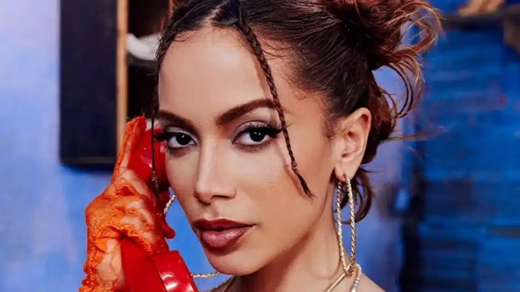 Foto de Anitta com maquiagem carregada, luvas vermelhas, segurando telefone também vermelho