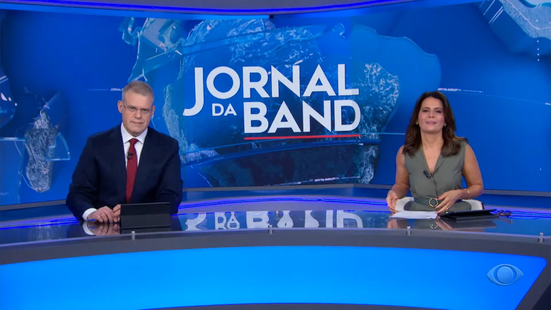 Foto dos jornalistas Eduardo Oinegue e Adriana Araújo na bancada do Jornal da Band