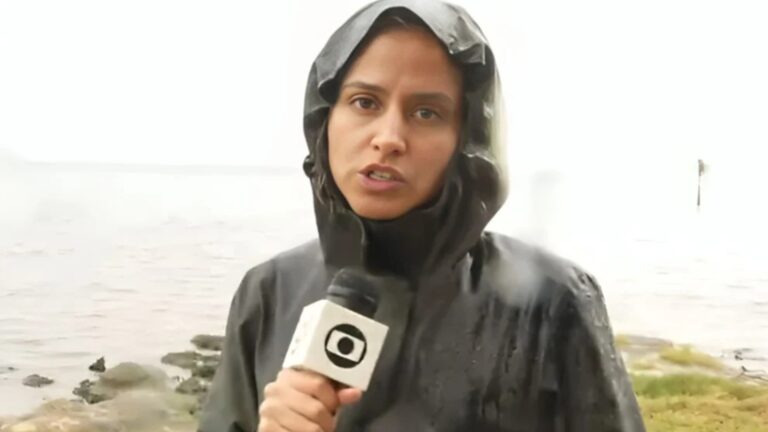 Foto da repórter Raquel Krähenbuhl com capa de chuva e microfone da Globo