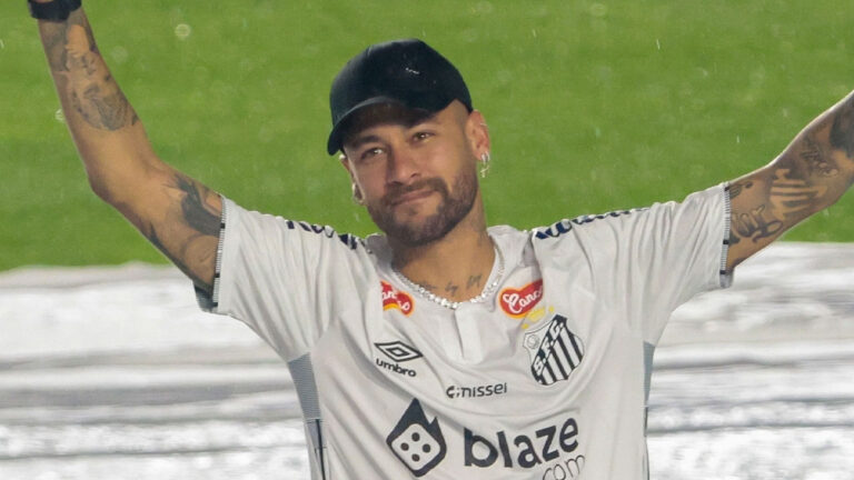 Neymar Jr. na Vila Belmiro usando a camisa do Santos, boné preto e braços erguidos, sorrindo durante evento sob chuva