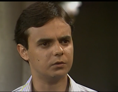 A imagem mostra Ricardo, personagem da novela Tieta, exibida pela TV Globo em 1989. Ele aparece com uma expressão séria e um olhar atento, sugerindo preocupação ou surpresa diante de uma situação