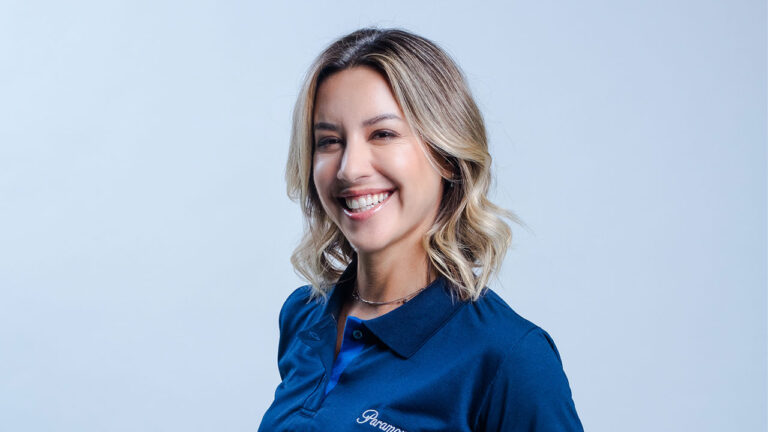 Cris Dias sorrindo em ensaio promocional com camisa azul da Paramount+ sobre fundo claro
