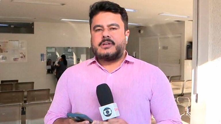 Geraldo Beckher, repórter da Globo, segurando microfone e celular em entrada de unidade de saúde