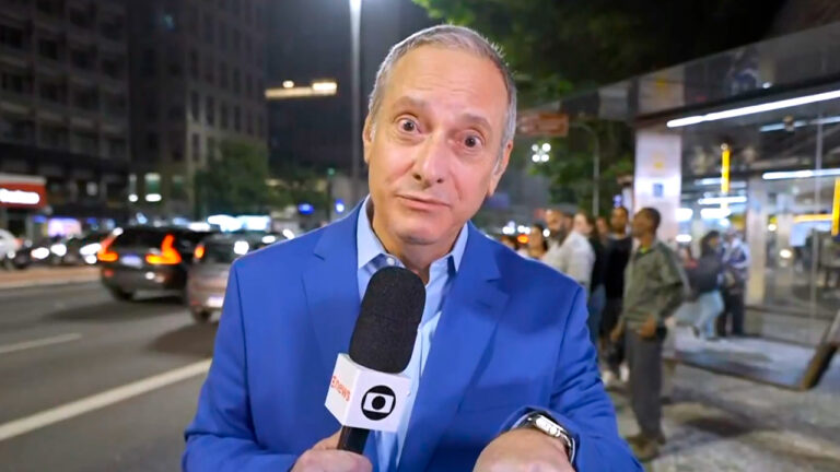 José Roberto Burnier segura microfone da Globo em participação ao vivo noturna na Avenida Paulista em São Paulo