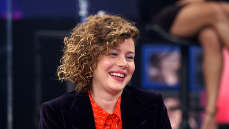 Leandra Leal sorrindo durante participação no programa Altas Horas, vestindo blazer roxo e camisa vermelha estampada