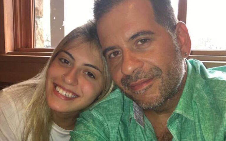 Leandro Hassum posa sorridente ao lado da filha, Pietra, em um momento de carinho. O ator usa uma camisa verde clara, enquanto Pietra aparece com os cabelos loiros soltos e camiseta branca, exibindo um sorriso aberto. A foto, registrada em ambiente interno com luz natural, transmite um clima de cumplicidade e afeto entre pai e filha.