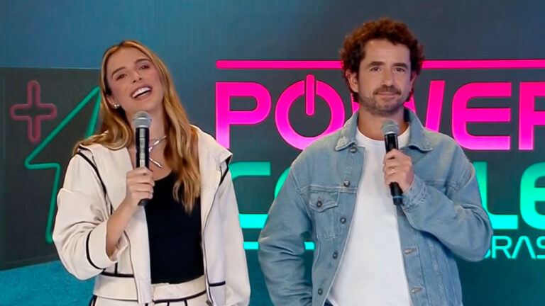 Rafa Brites e Felipe Andreoli falam ao público com microfones em frente ao telão com logo do Power Couple Brasil