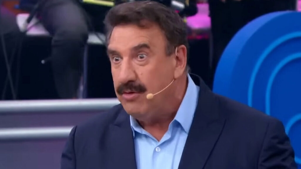 Ratinho durante apresentação do Programa do Ratinho no SBT usando paletó azul e microfone de lapela no palco