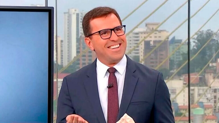 Rodrigo Bocardi sorri durante apresentação do Bom Dia São Paulo com vista da cidade ao fundo