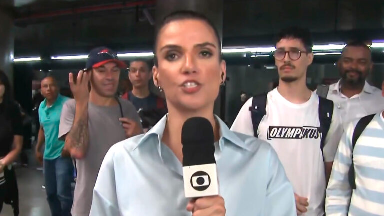 Sabina Simonato segura microfone da TV Globo durante entrada ao vivo em estação de metrô movimentada