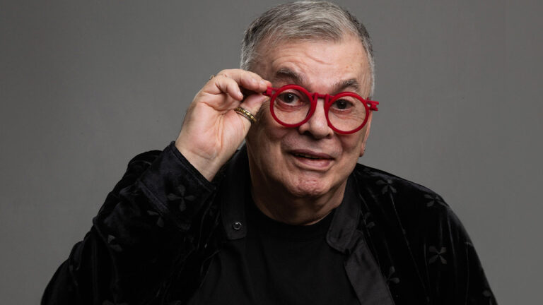 Walcyr Carrasco posa para foto usando óculos vermelhos e roupa preta diante de fundo cinza