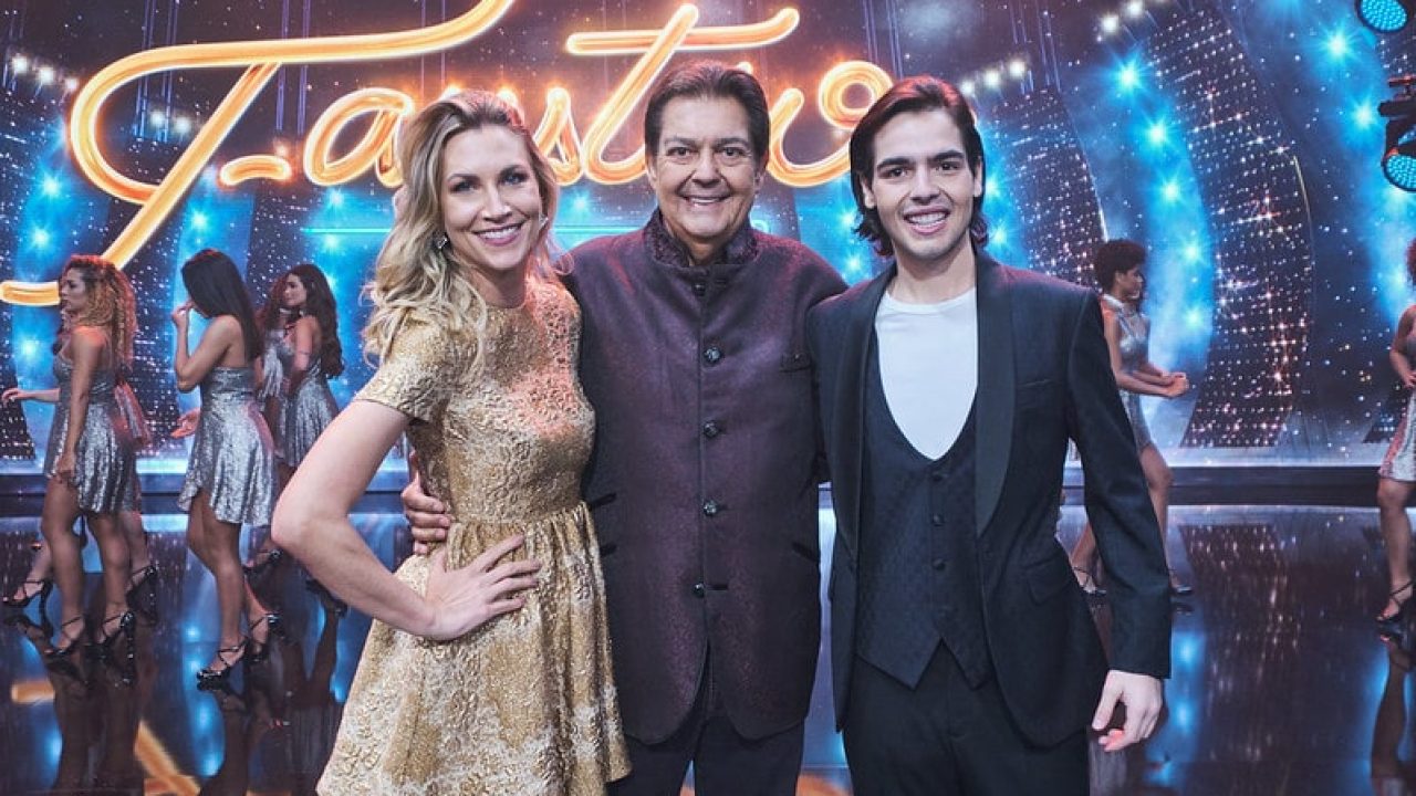 Imagem com foto de Anne Lottermann, Fausto Silva e João Guilherme Silva no palco do Faustão na Band