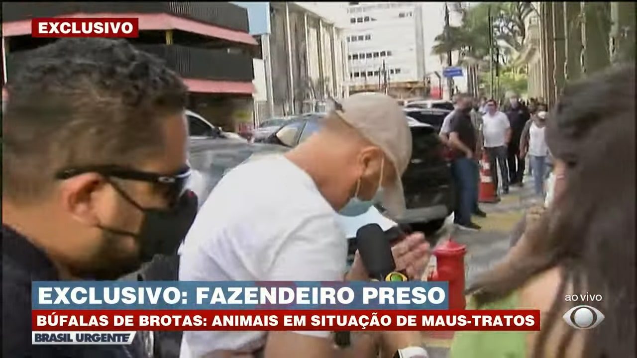 Imagem com foto do momento em que a equipe da Band é agredida na porta de uma delegacia