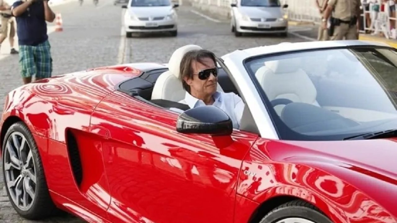 Imagem com foto do cantor Roberto Carlos dirigindo seu carro vermelho