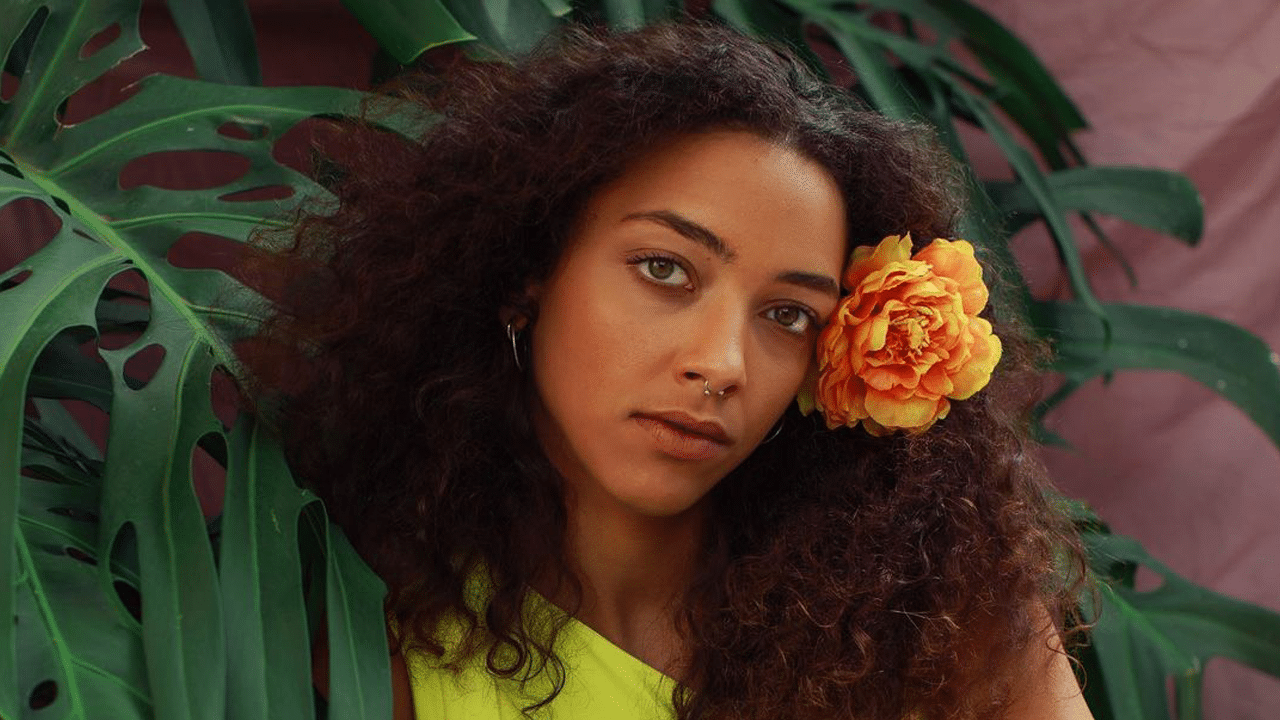 Alice Carvalho em foto postada nas redes sociais. Ela está com uma flor da cor laranja nos cabelos