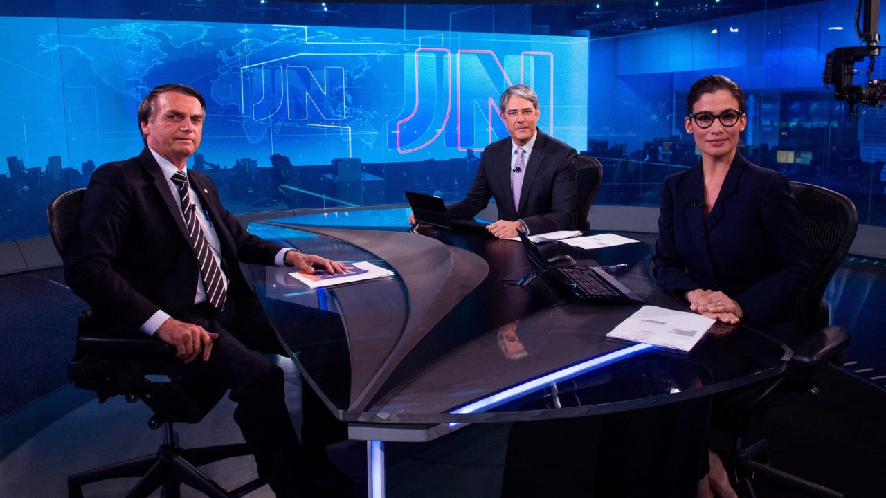 Imagem com foto de William Bonner e Renata Vasconcellos entrevistando Jair Bolsonaro no Jornal Nacional