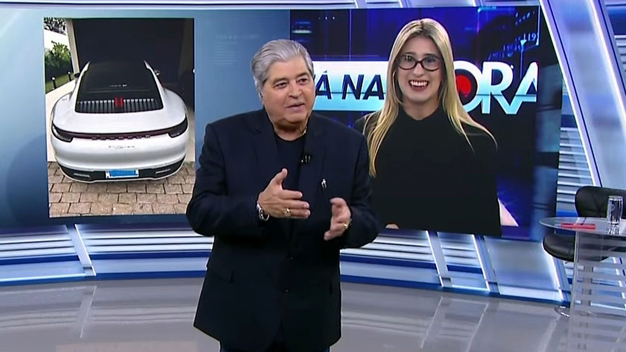 Datena apresenta o programa Tá na Hora no SBT com a repórter Nicole Bonentti no telão ao fundo