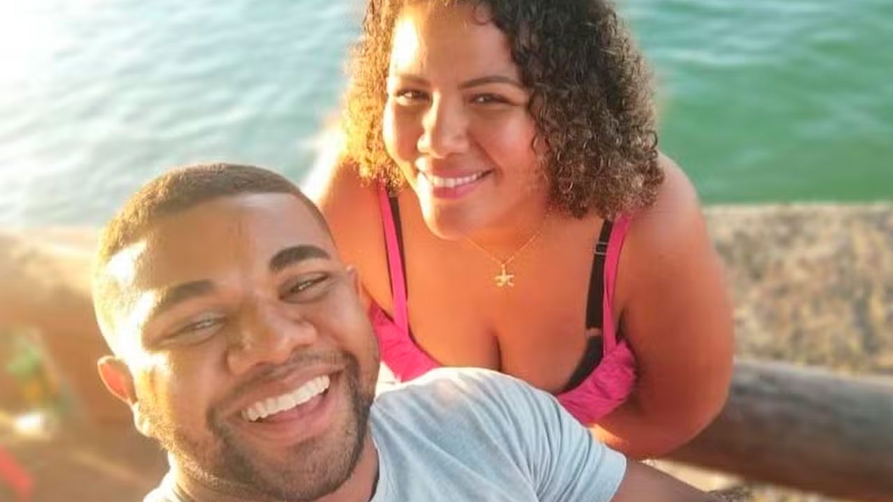 Davi Brito e Mani Rego sorrindo juntos em área externa com vista para o mar ao fundo