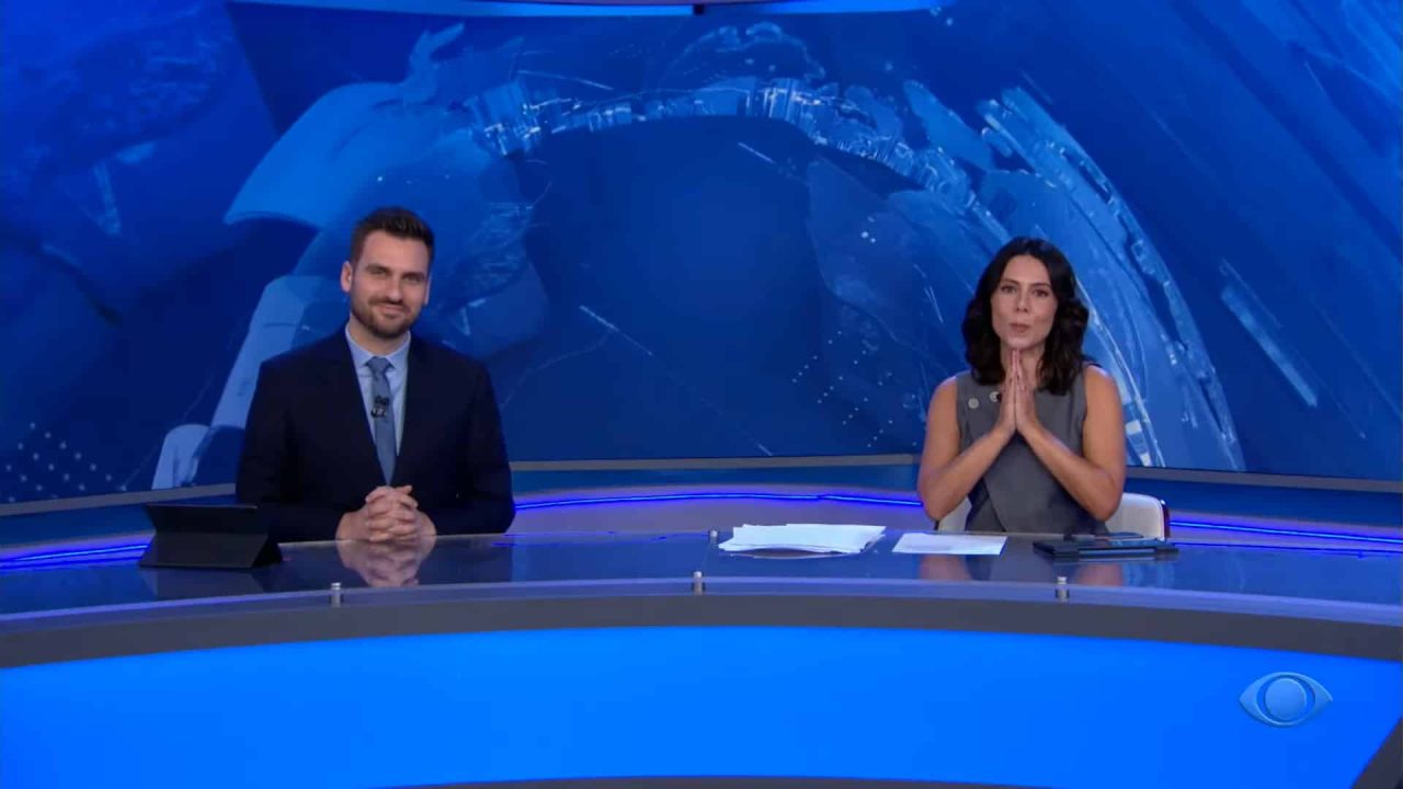 Foto de Douglas Santucci e Paula Valdez na bancada do Jornal da Band