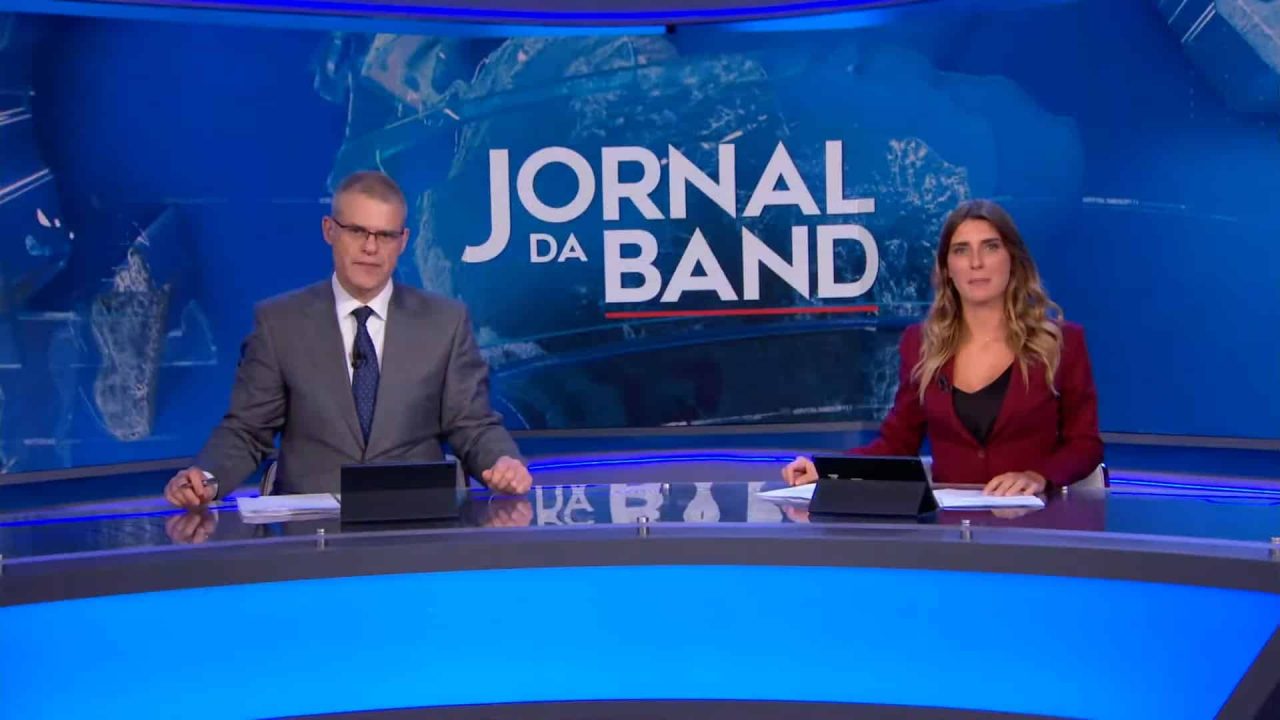 Foto dos jornalistas Eduardo Oinegue e Joana Treptow na bancada do Jornal da Band