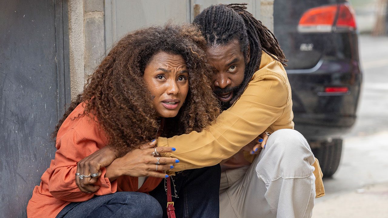 Madalena e Jão agachados e assustados durante confronto na Vila Cambucá em cena da novela Volta por Cima da Globo