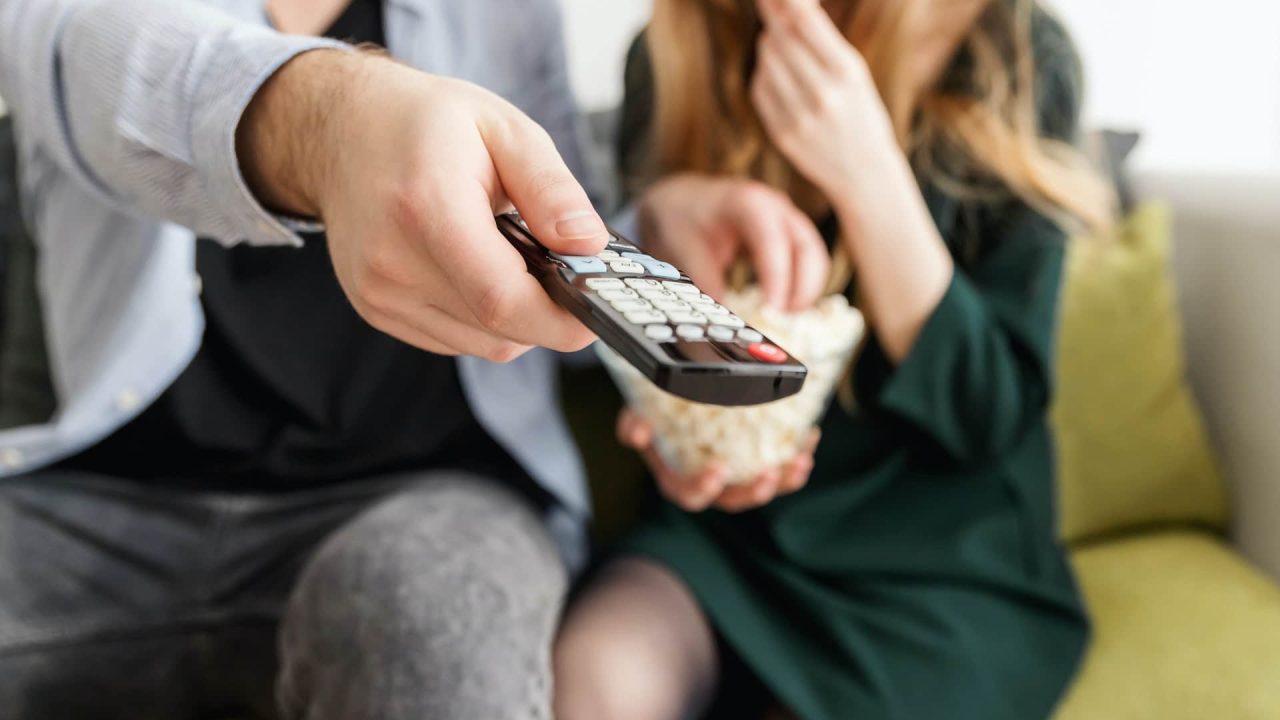 Imagem com foto de pessoas assistindo televisão apontando o controle remoto