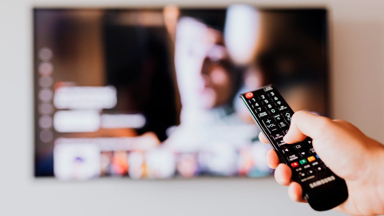 Imagem com foto de controle na frente de uma tela de TV por assinatura