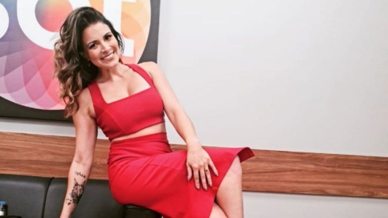 Foto de Renata Del Bianco de vestido vermelho decotado em frente ao logo do SBT