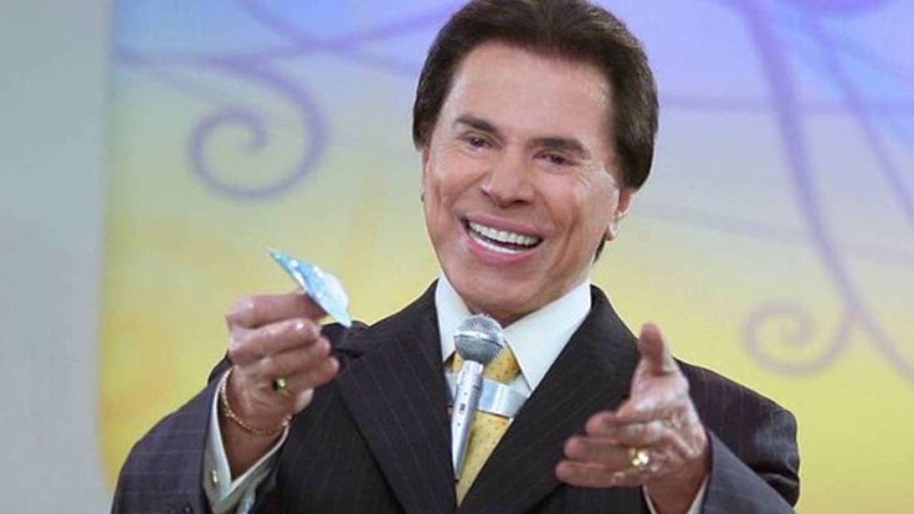 Foto do apresentador Silvio Santos olhando para uma nota de dinheiro