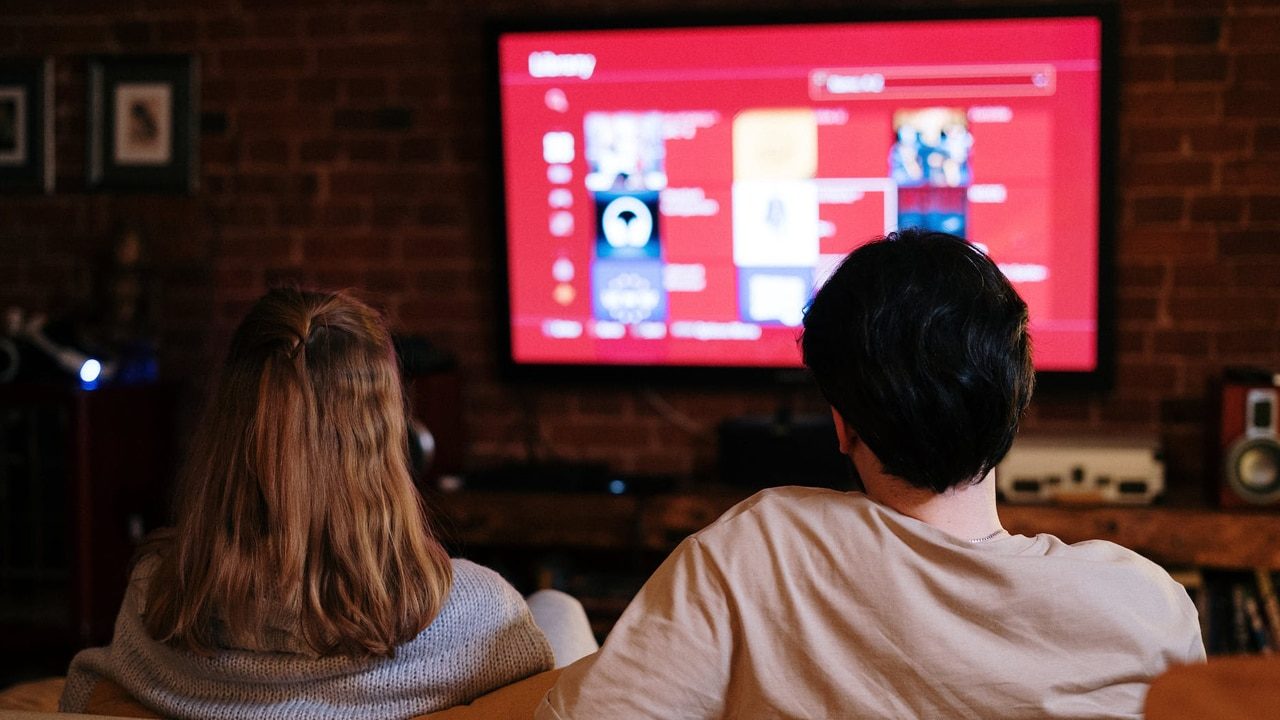 Casal sentado em um sofá na frente de um aparelho de TV por assinatura