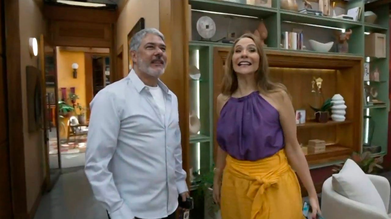 William Bonner e Maria Beltrão sorrindo no cenário do É de Casa da TV Globo em frente a estante decorada do estúdio